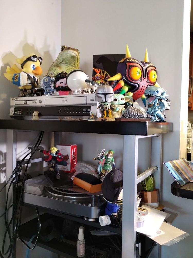 Shelving unit with 2 tiers. Filled with figurines like a Blue Eyes White Dragon and Alpha from Final Fantasy XIV