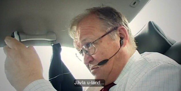 Dåvarande statsminister Göran Persson sitter i baksätet på en bil och håller upp en mobil framför sig och tittar irriterat på den över kanten på sina glasögon. Persson har en öronsnäcka i örat med en sladd som löper till mobilen.

En textremsa talar om vad Persson säger: "Jävla  u-land..." 