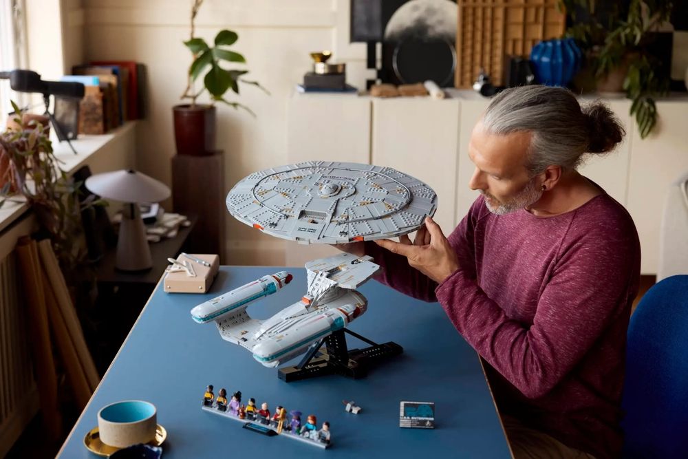 En man sitter vid ett bord och bygger en legomodell av skeppet Enterprise från Star Trek.  Modellen är nästan lika stor som hans överkropp. 