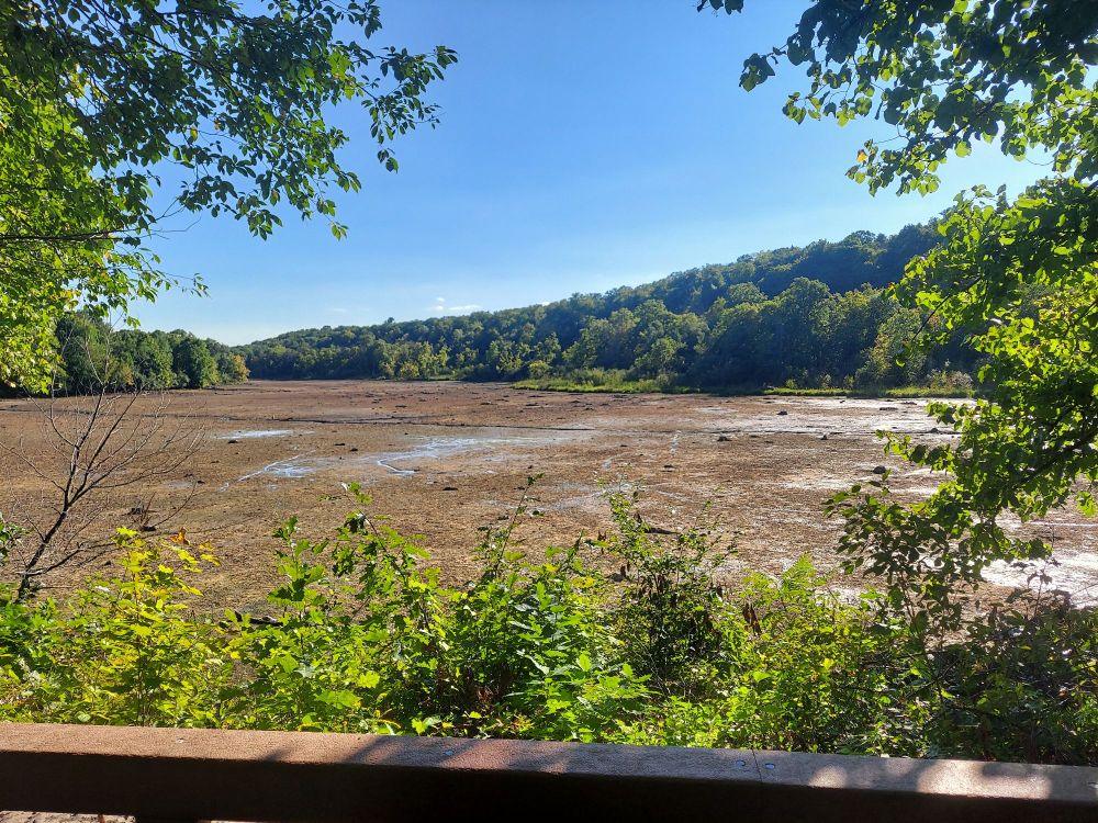A dry lake bed with lush, forested hills in the background