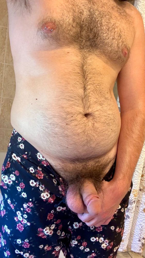 Me shirtless, pulling my swim trunks down with my left hand exposing my bushy cut dick and balls