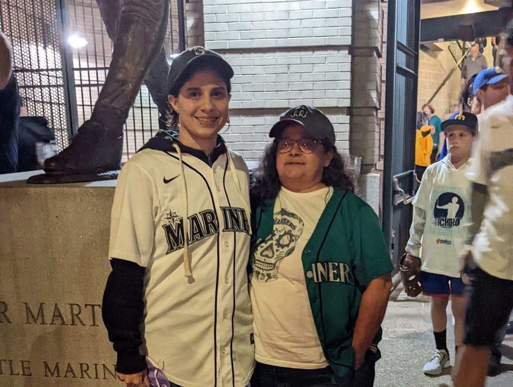 Jeanine and her mom wearing Mariners gear in front of the Edgar Martinez statue (unseen, but should be known: they are both wearing Edgar jerseys) outside of T Mobile Park 