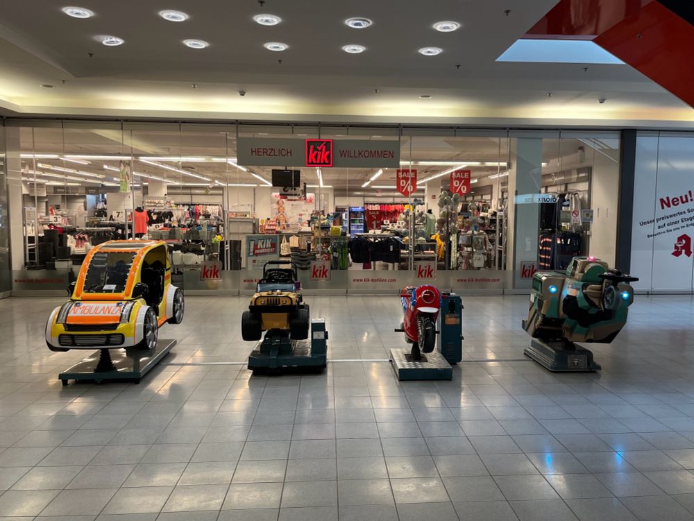 fahrzeug replikas für kinder vor einer kik filiale: krankenwagen, geländewagen, motorrad, panzer