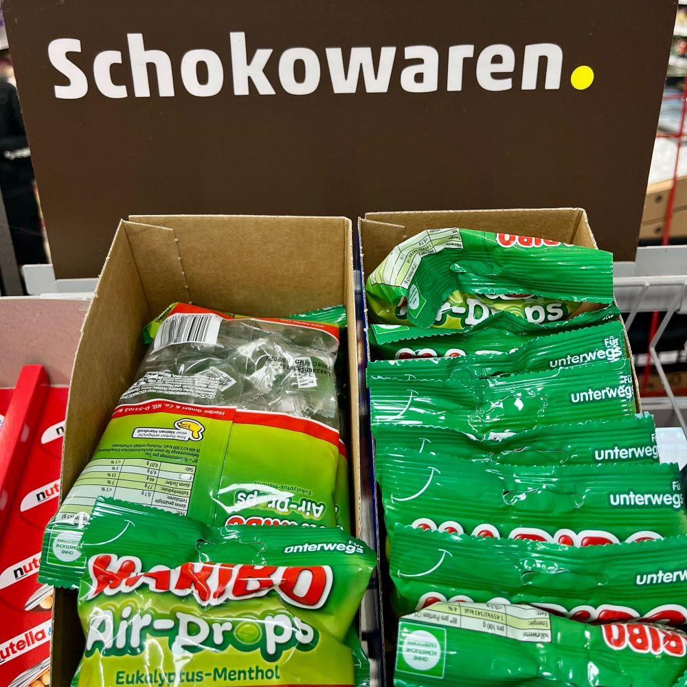 ein schild auf dem „schokowaren“ steht, davor zwei kassenschieber mit haribo air drops (eukalyptus  bonbons)