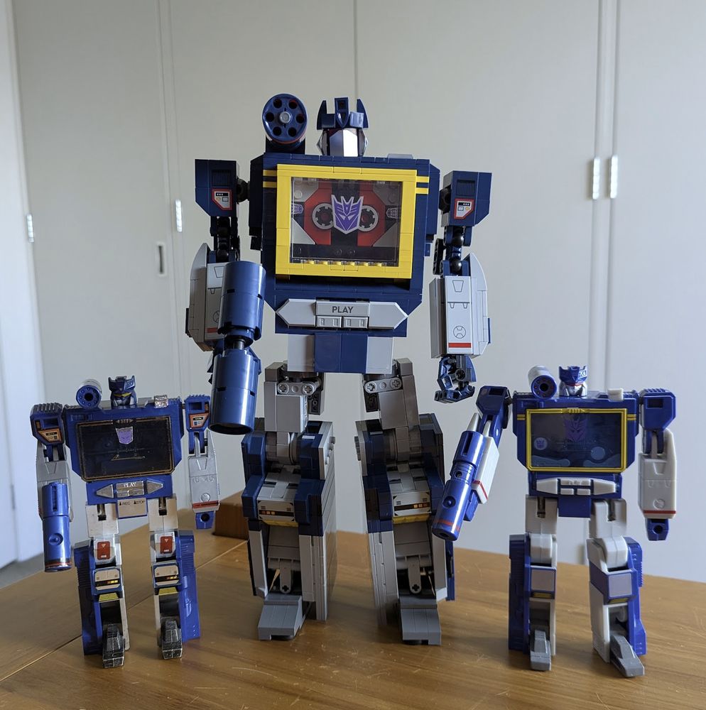 Photograph of three different versions of the Transformer "Soundwave" in robot mode.

On the far left is the 1st Generation (1984 version) of the toy.  In the middle is the new Lego version (about twice the size) and on the right is the 40th Anniversary edition of the toy, which mimics the original G1 version except in colour scheme - switching silvers for greys and adding yellow.