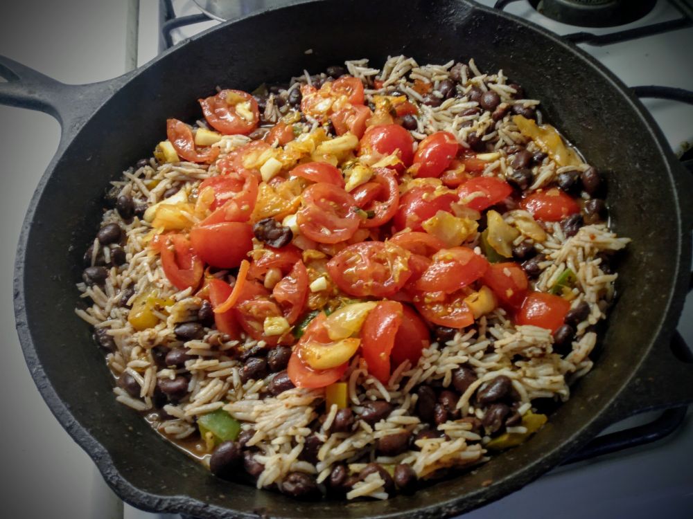 Black beans, basmati rice, fried bell peppers, with diced tomatoes and garlic, vinegar and olive oil in a black iron skillet. 