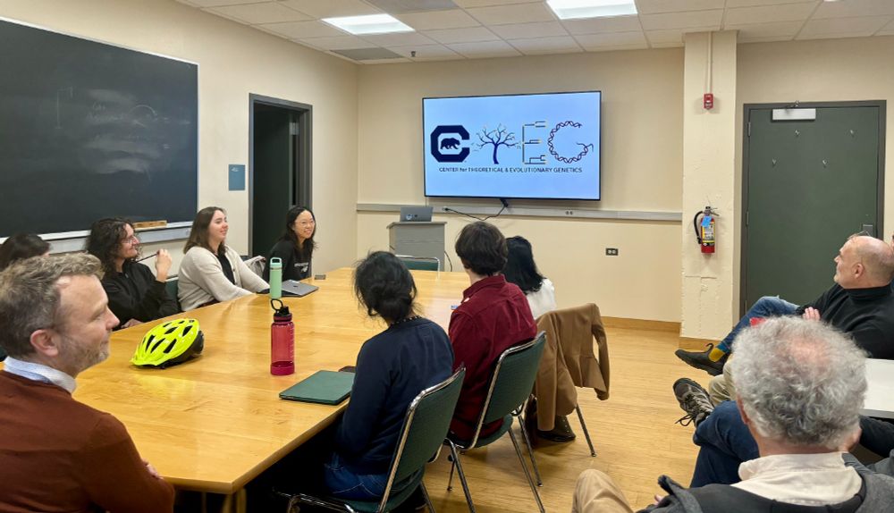A group of researchers sits around a table and looks at a monitor displaying logos for CTEG during a seminar.