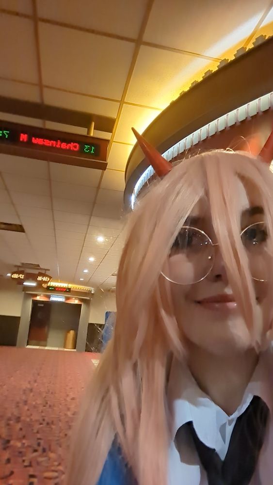 A selfie of me cosplaying Power from Chainsaw Man in a theater, with the title display for the Chainsaw Man: Reze Arc visible