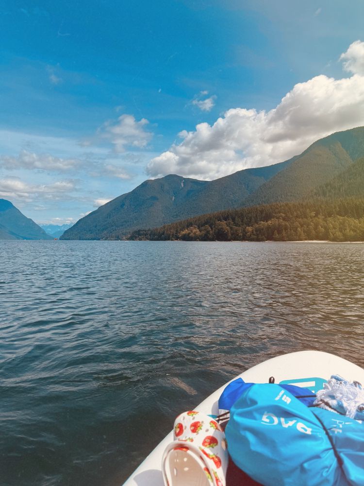 Picture of the front of a paddle board in the middle of a lake with mountains in the background 