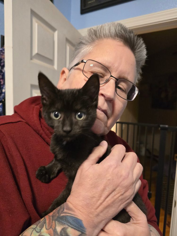 Old woman holding a young black kitten named Ducky; he's 14weeks and only 2.98 pounds.