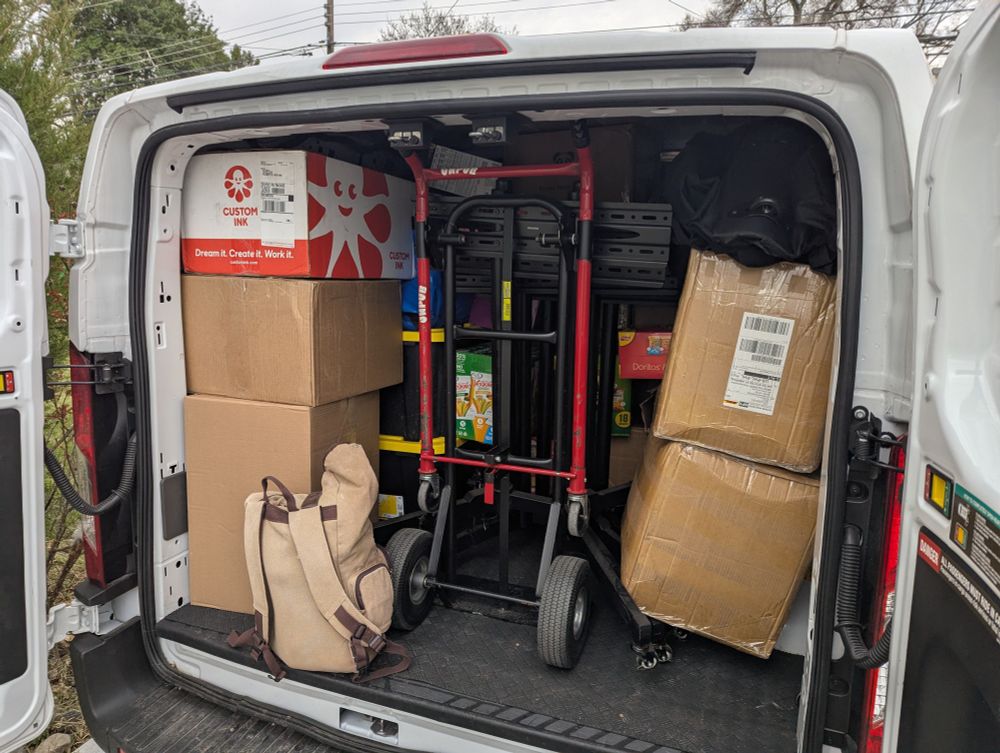 The rear doors of a packed Uhaul van are open to reveal boxes and a dolly.