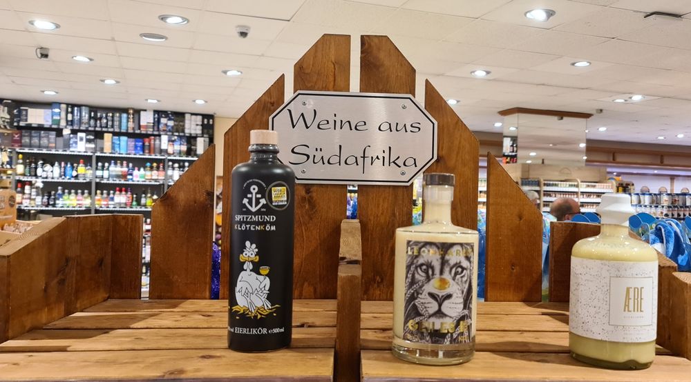 Im Supermarkt. An einem Holzregal hängt ein Schild mit der Aufschrift "Weine aus Südafrika". Im Regal zu sehen sind aber nur drei verschiedene Sorten Eierlikör.
Immerhin eine hat einen Löwen auf dem Etikett.