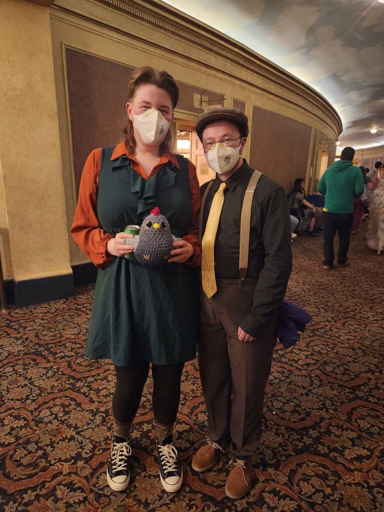 @queerposting and I standing in the lobby of the Orpheum Theatre. We are both dressed as Stardew Valley characters -- she is Marnie, and I am Mayor Lewis
