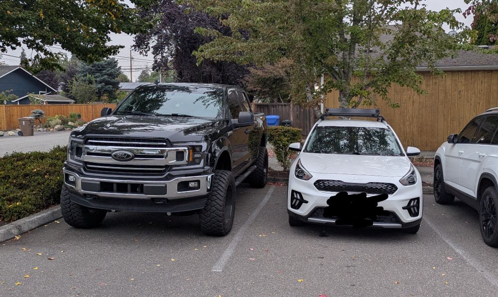 A large black Ford truck next to a much smaller white Kia. 