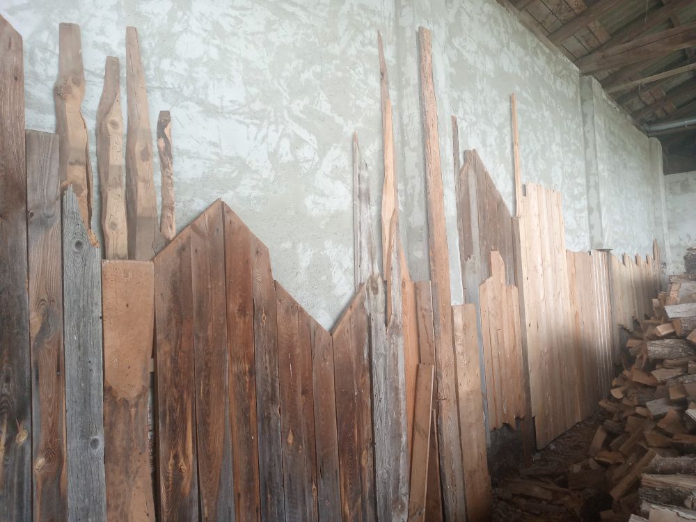 Die hintere Wand des Wirtschaftsgebäudes eines Bauernhofes, zum Teil mit alten Brettern verkleidet. Die Anordnung der Bretter zeichnet eine Großstadt-Skyline nach.