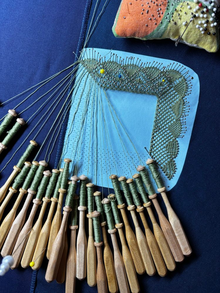 Bobbin lace boarder being made. Many bobbins hanging with green thread. Green torchon lace on a blue mat. 