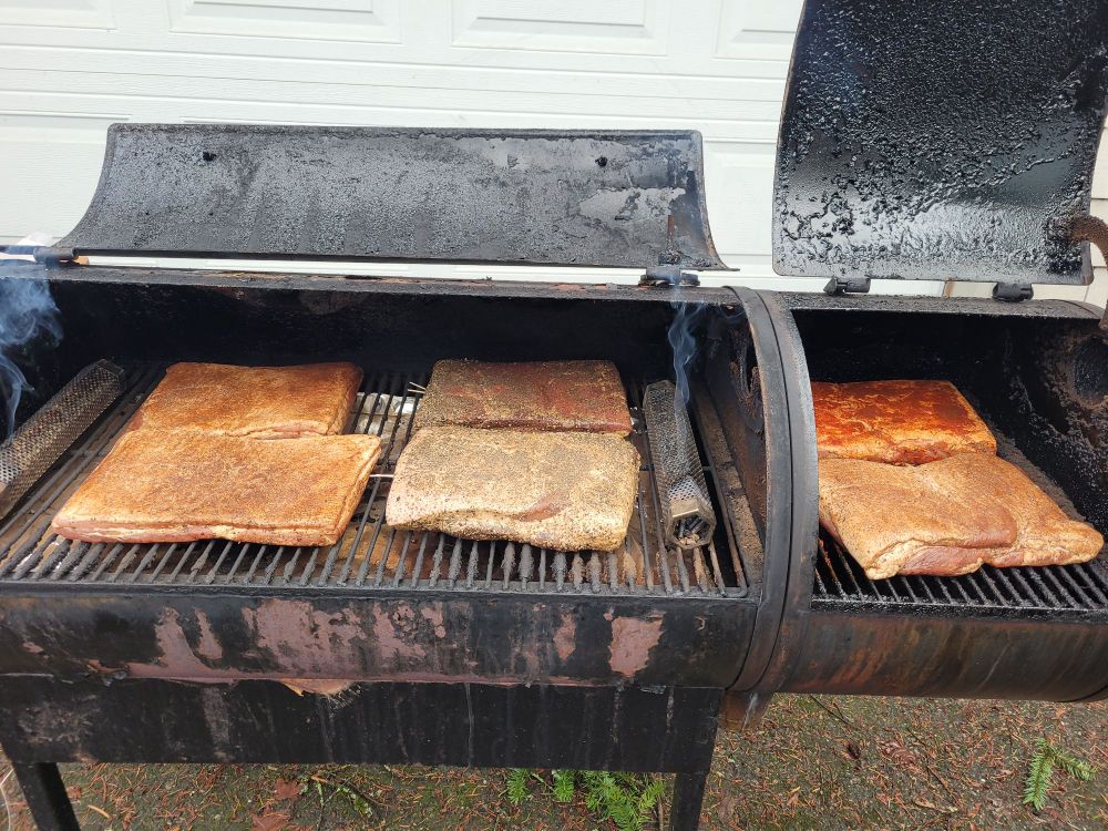 A smoker with 6 slabs of bacon and smoke tubes filling it up.