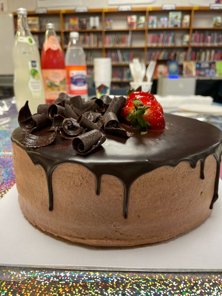 A luscious Chocolate cake in the foreground, with chocolate curls and two strawberries 