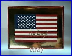 A small American flag desecrated and defaced; signed by donald trump in gold sharpie.