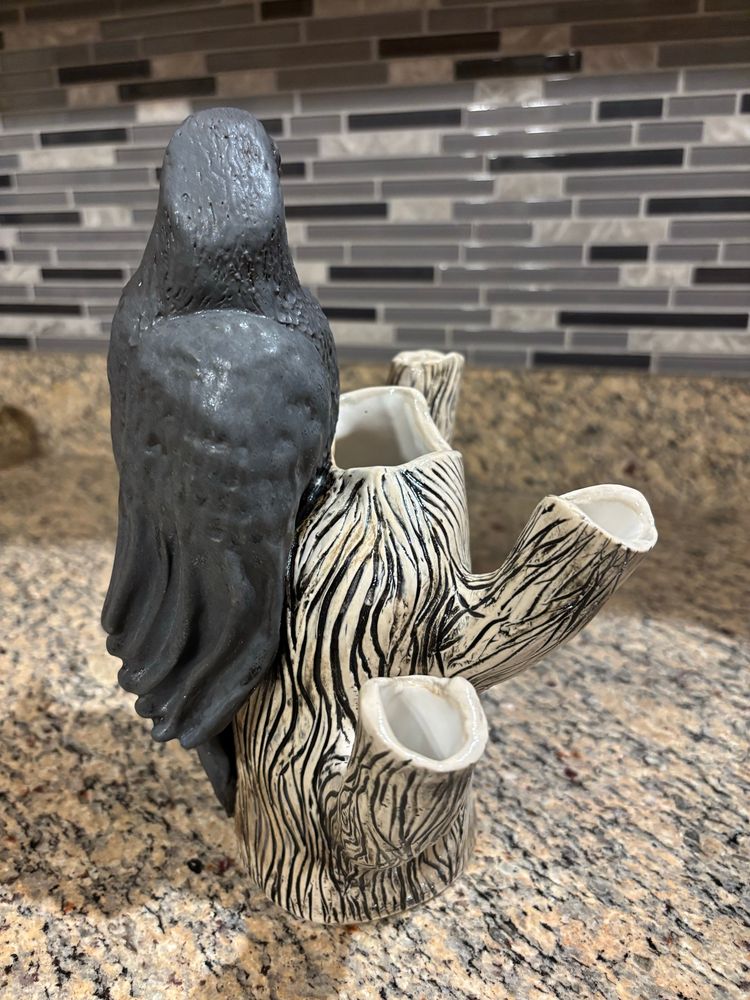 Hand built ceramic raven perched on a white dead tree. Vase made of clay