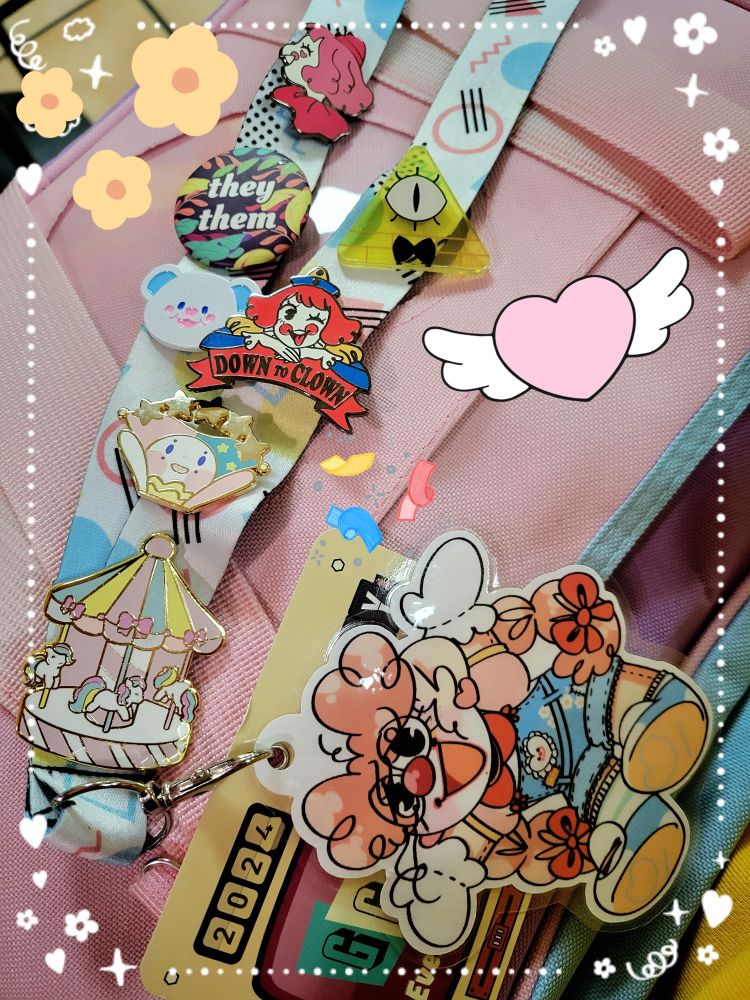 Lanyard with badge art of a clown over a con vadge and various pins on it. Including multiple clowns, a carousel, a they/them pronoun button, bohug the bear, and bill cipher.