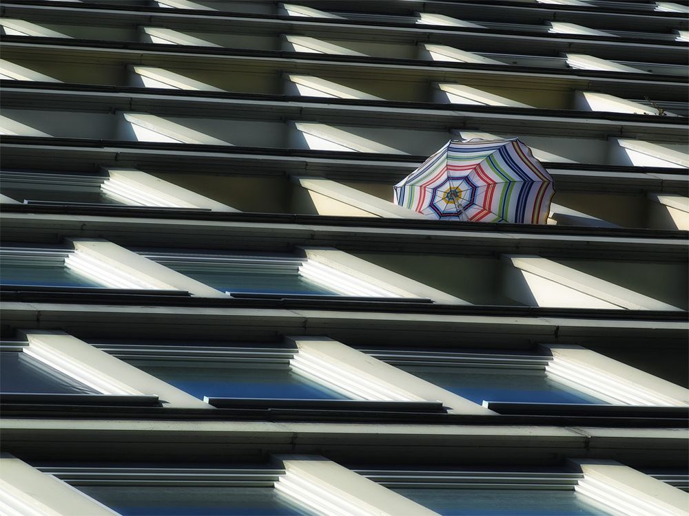 Hochhausfassade mit einem bunt gestreiften Sonnenschirm