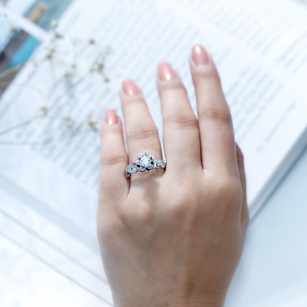 A stunning Moissanite Floral Engagement Ring featuring a 5mm round brilliant Moissanite in a prong setting, surrounded by delicately crafted petals adorned with smaller Moissanites. The nature-inspired flower design blends vintage elegance with modern sparkle, symbolizing love and timeless beauty.