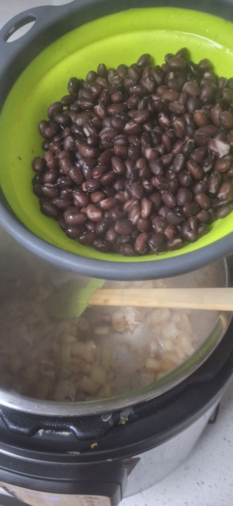 a colander of rinsed and cooked black beans over an instapot that has sautéed onions in it 