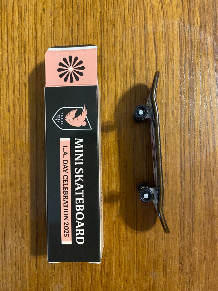 A photograph of a side view of a toy skateboard and the box that it came in. The box says mini skateboard with the angel city football club logo