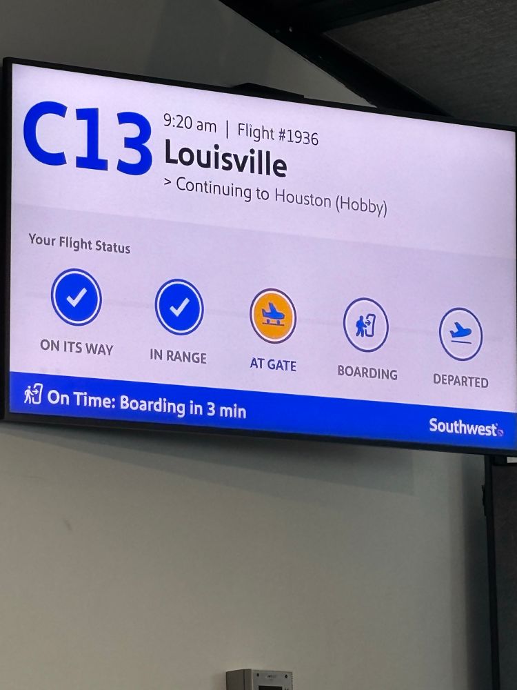 An airport sign for a flight to Louisville, KY indicating it will be momentarily boarding