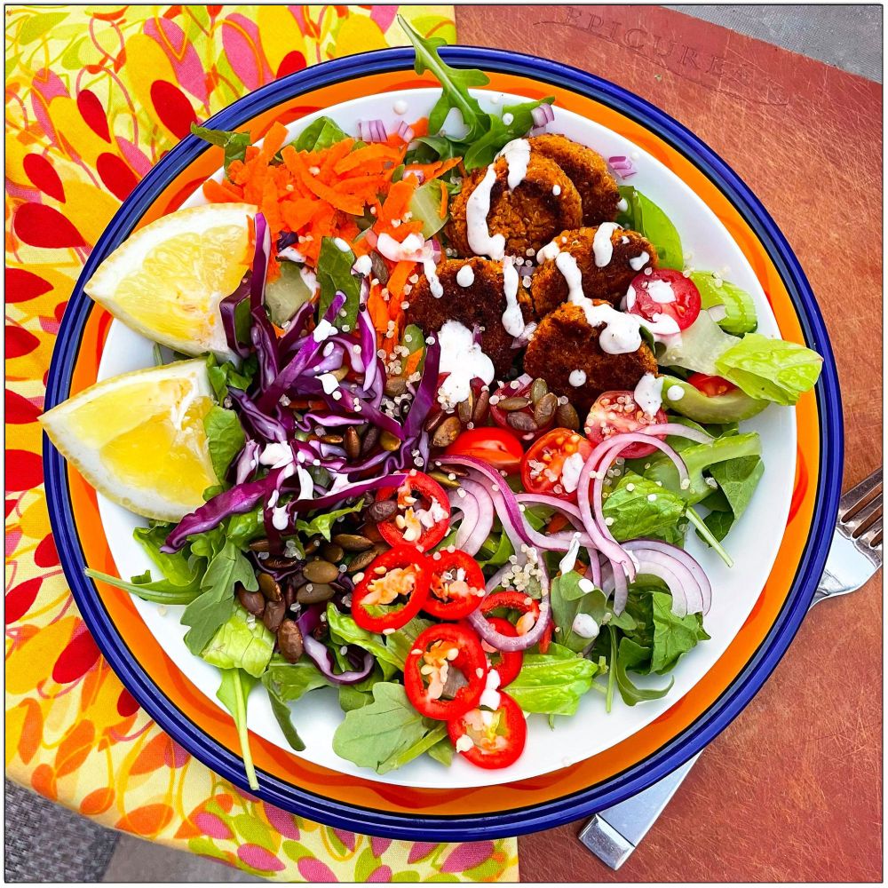 Salad with carrots, purple cabbage, red onions, fresno peppers, pepitas, and tomatoes on a bed of greens.