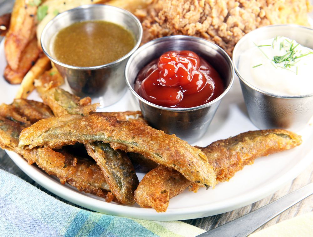 A white plate showing battered pickles with three dipping sauces.