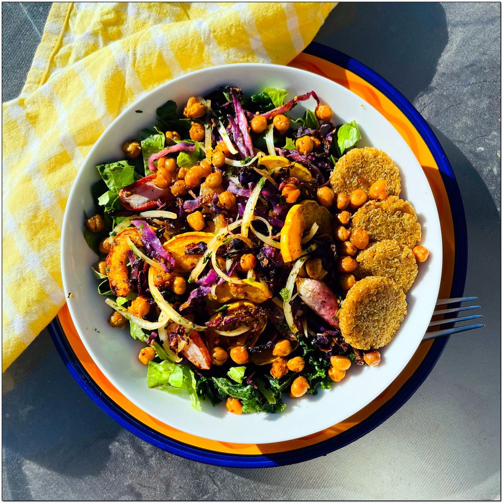 A salad bowl with different colored veggies and a side of quinoa patties. 