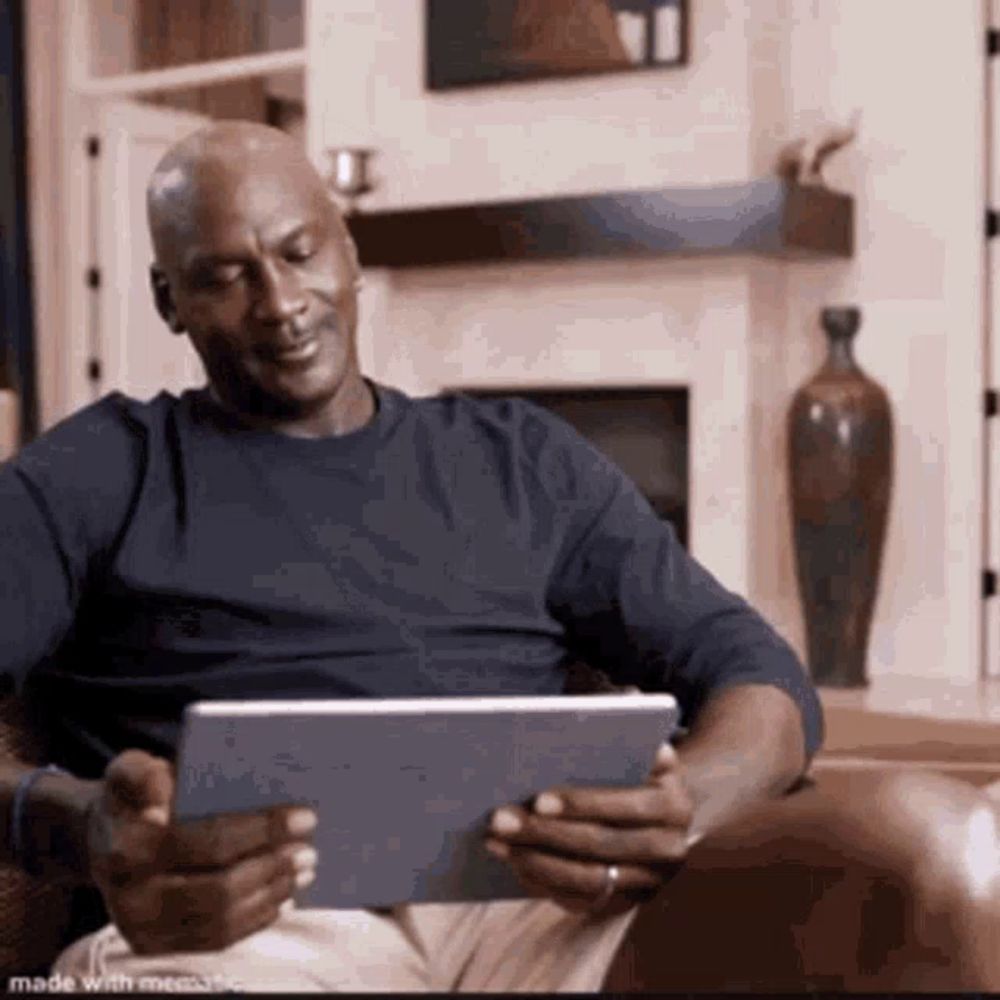 michael jordan is sitting on a couch looking at a tablet computer .