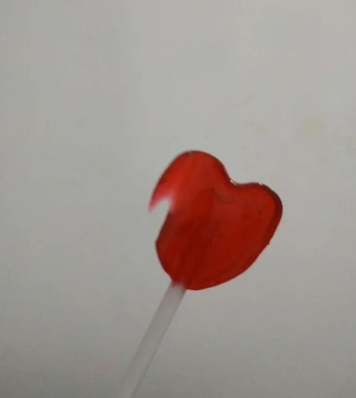 A blurry picture of a heart shaped red lollipop with part of its side having melted into a sharp hook of doom and death and disease.