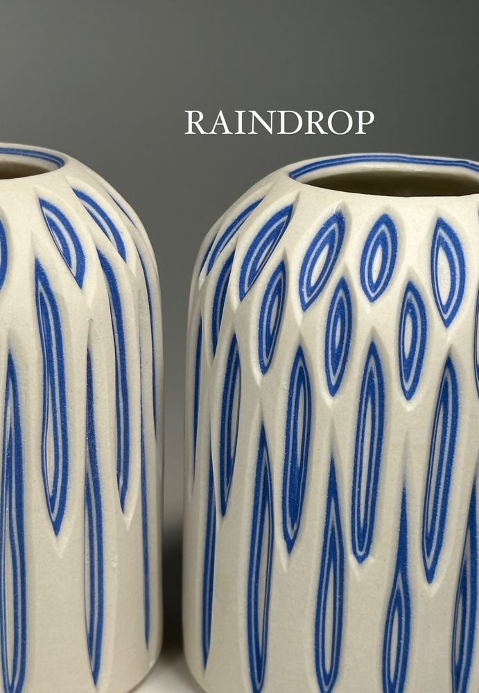 A small, canister bud vase with a white exterior and vertical carvings revealing layers of blue - the colorway is called "Raindrop"