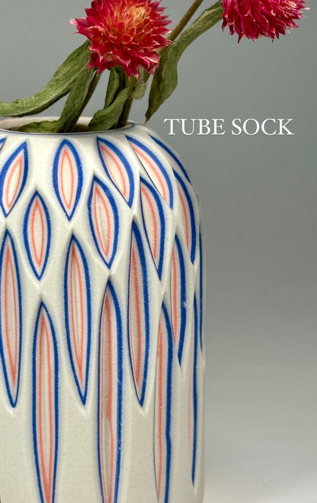 A small, canister bud vase with a white exterior and vertical carvings revealing a layer of blue and a layer of red - the colorway is called "Tube Sock"