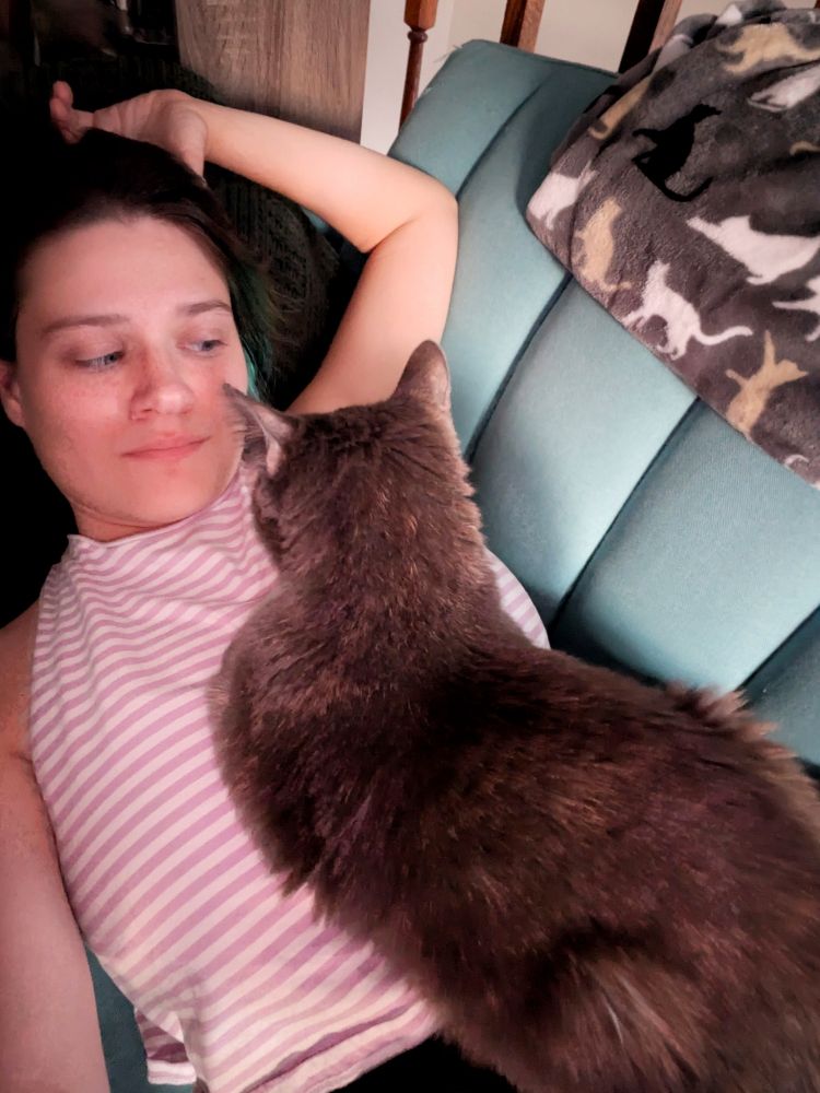 Andrea laying on a couch with a gray cat snoozing on her chest 