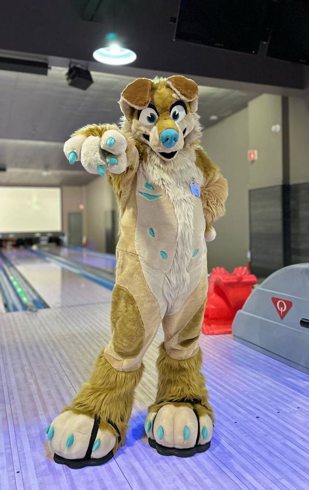 Golden retriever fursuiter in a bowling alley pointing at the camera