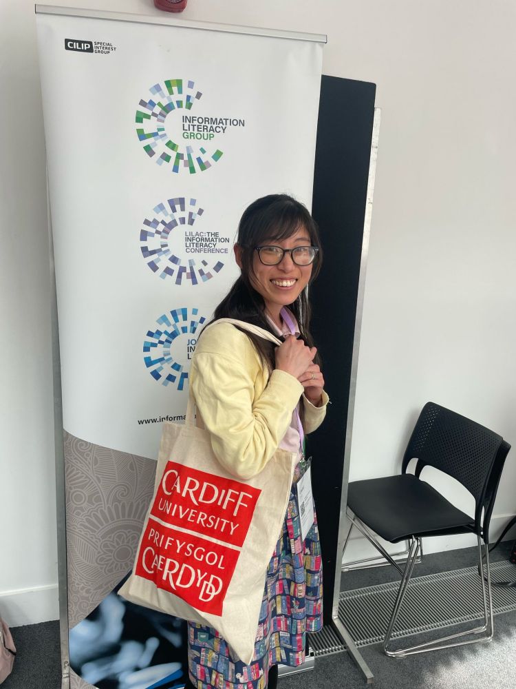 Yuri Watanabe holding a large Cardiff University tote bag containing gifts that she has won at the LILAC 2025 exhibition. 