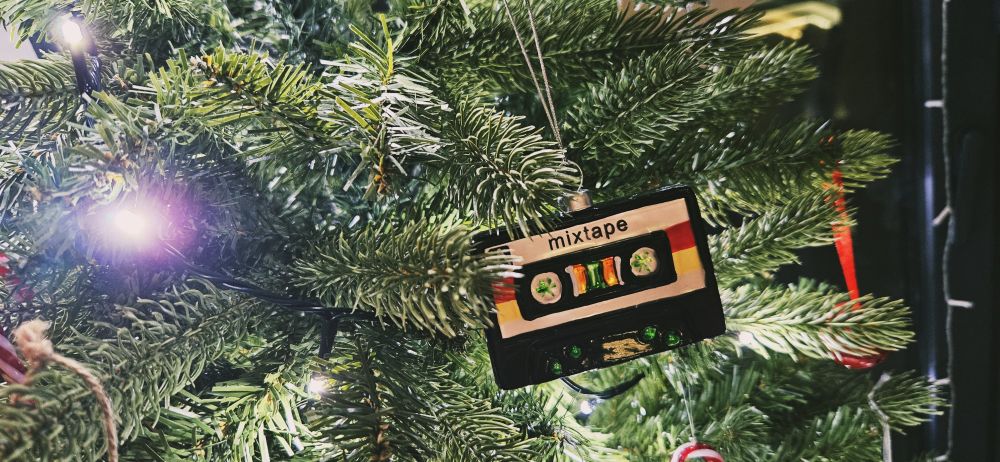 Close up of a Christmas tree decoration, hanging on a tree surrounded by sparkling lights, of a cassette tape - which reads "mixtape".