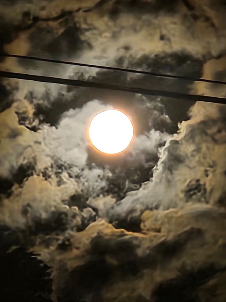 Photo of the full moon, clouds, and power lines. 
