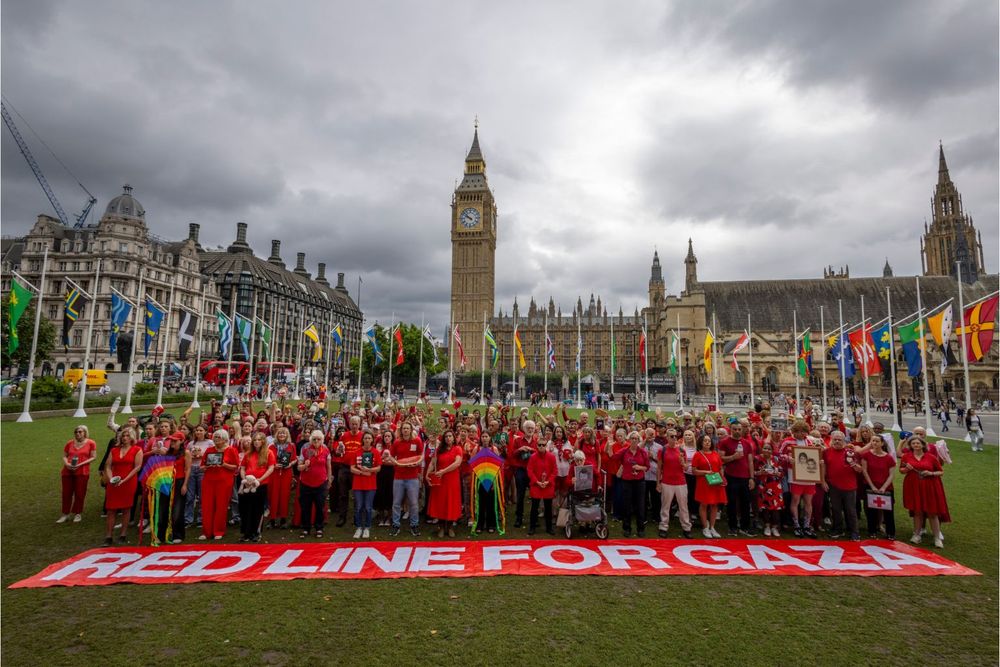 Group of people stand outside Parliament with a banner that reads Red Line for Gaza.