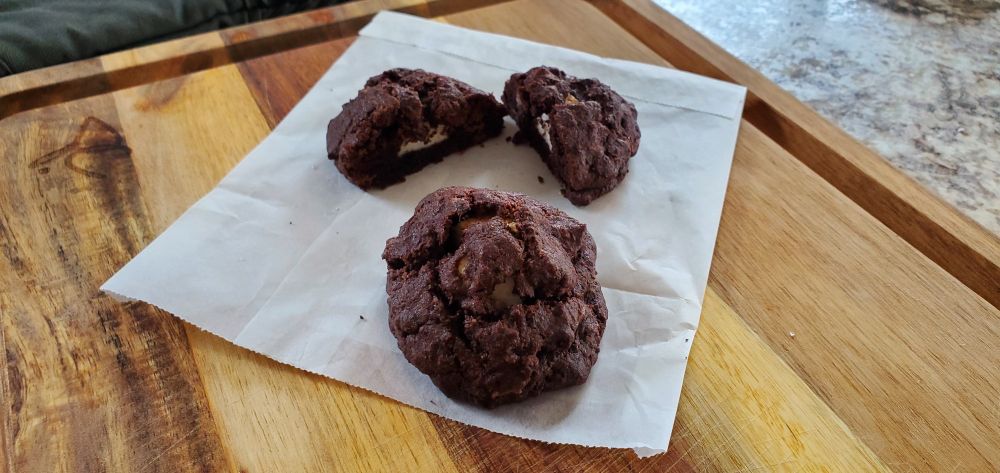 Two chocolate cookies, one cut in half to reveal marshmallow in the middle