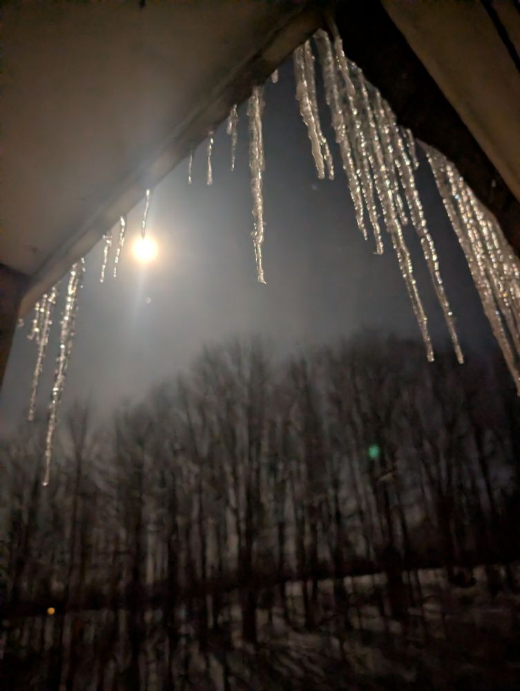 The moon reflecting on the icicles with trees on the hill in the background.