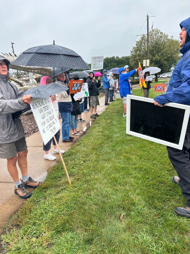 A photo of a protest in the rain with demonstrators chanting.