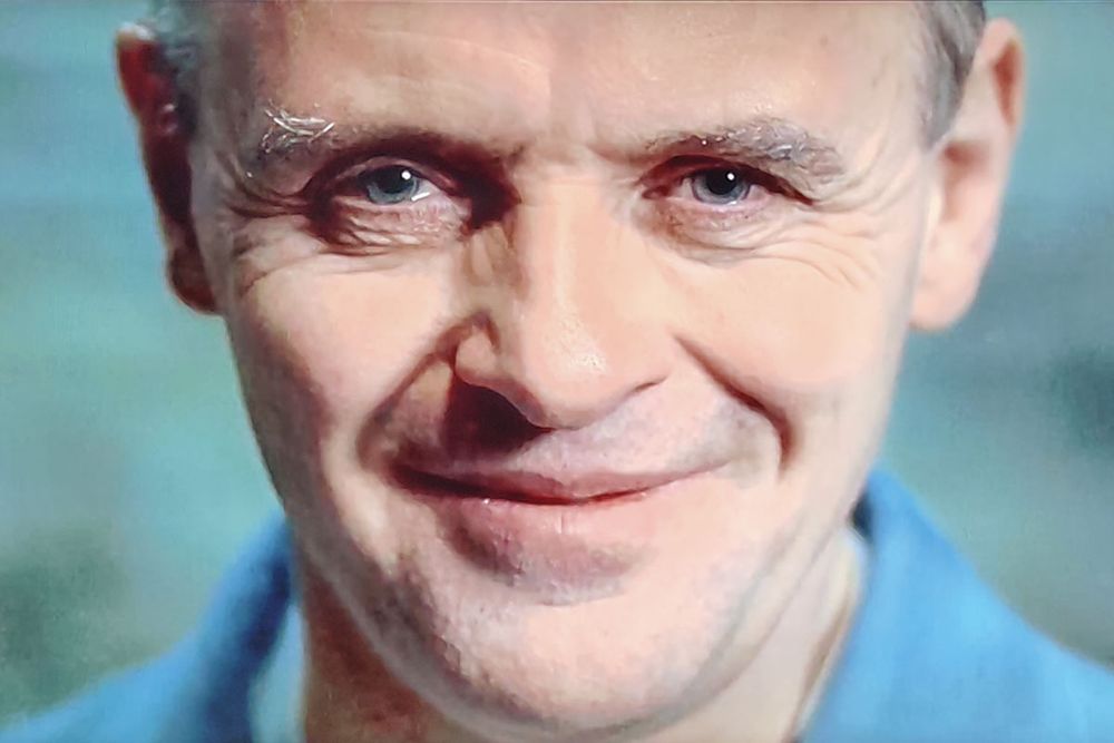 closeup of Anthony Hopkins as Hannibal Lecter smiling and looking at camera