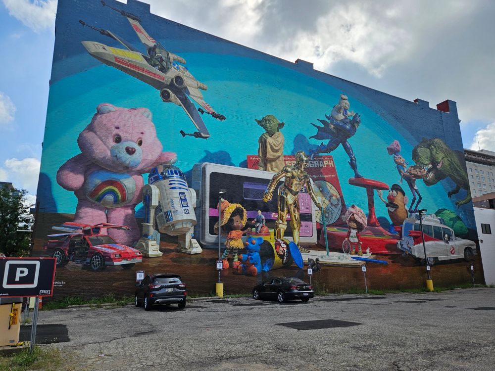 A mural depicting Kenner toys seemingly come to life, including a Care Bear, R2-D2, an X-Wing being piloted by Boba Fett, Yoda, C3PO, Strawberry Shortcake, Mr. Potato Head, and others.