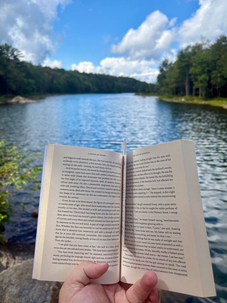 Photograph of my hand holding up a book in front of another lake view.