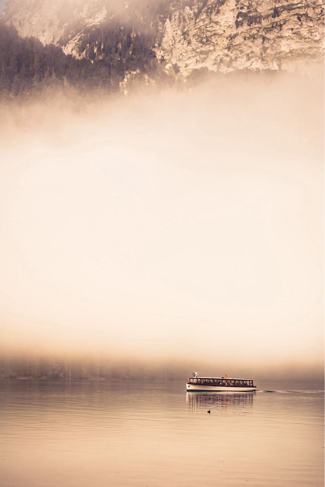 Ein elektro-betriebenes Motorboot auf dem Königssee. Dahinter eine große Nebelbank. Am oberen Bildrand ist eine Felswand und einige Bäume zu erkennen